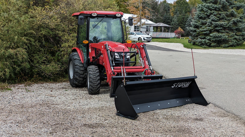 Storm angle snow blade mounted on a red compact tractor, side view with the blade angled to the right