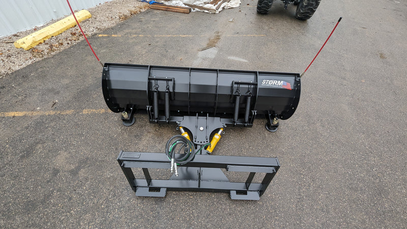 Storm angle snow blade laid out on pavement beside its mount frame, showing the moldboard and the hose set