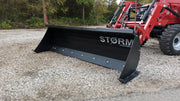 Storm angle snow blade on a red tractor loader on gravel, angled view across the moldboard face