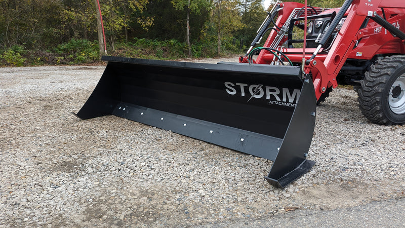Storm angle snow blade on a red tractor loader on gravel, angled view across the moldboard face