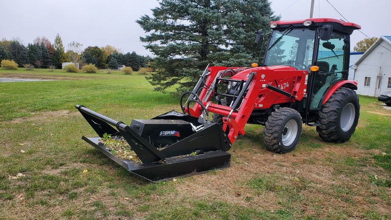 Storm 60 inch brush cutter mounted on a red compact tractor loader, working through grass on an open lawn