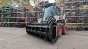 Storm HD rake and brush grapple mounted on a white skid steer, side view on a gravel yard