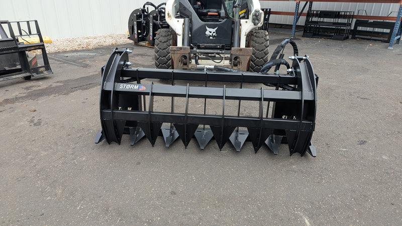 Storm HD rake and brush grapple on a skid steer, head-on view across the full width of the serrated tines