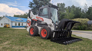 Storm HD root and brush grapple on a white skid steer on grass, tines extended forward