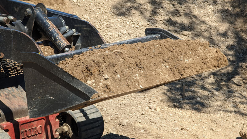 Storm mini bucket on a Toro Dingo track loader carrying a load of soil, side view of the filled bucket