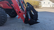 Storm rake and brush grapple mounted on a red compact tractor loader, side view with the serrated tines curved down