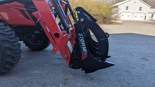 Storm rake and brush grapple mounted on a red compact tractor loader, side view with the serrated tines curved down
