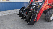 Storm rake and brush grapple on a red tractor, three-quarter view of the tine bank beside a building