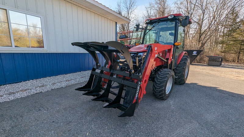 Storm 48 inch rake and brush grapple on a red tractor beside a building, head-on view across the tine bar
