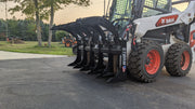 Storm rake and brush grapple mounted on a white skid steer on a driveway at dusk, side view