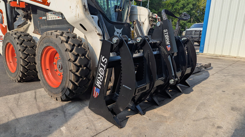 Storm rake and brush grapple on a white skid steer, three-quarter view with the serrated tines forward
