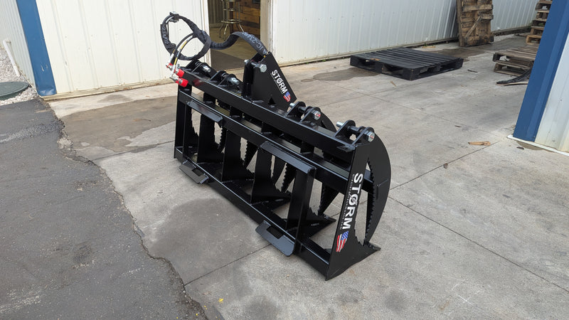 Storm rake and brush grapple set on pavement beside a building, three-quarter view of the tine bank