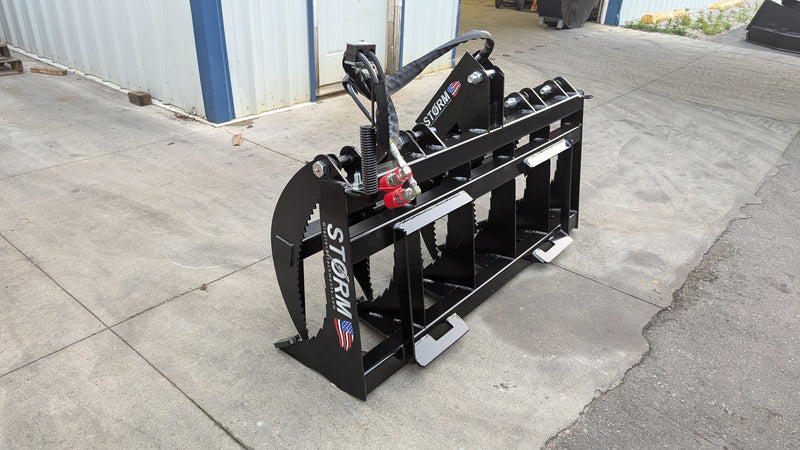 Storm rake and brush grapple on pavement, angled view showing the frame, tines, and top cylinder