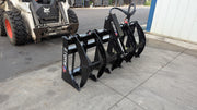 Storm 60 inch single cylinder rake and brush grapple on pavement beside a skid steer, angled view of the tines and arms