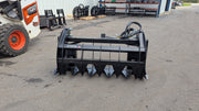 Storm 60 inch two cylinder rake and brush grapple on pavement, straight-on view across the tine bar and the frame
