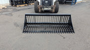 Storm rock bucket on pavement with a skid steer behind, front view of the spaced tines