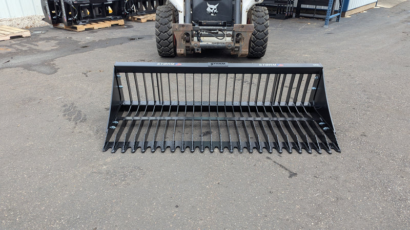 Storm rock bucket on pavement with a skid steer behind, front view of the spaced tines