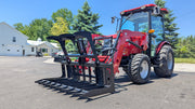 Storm root and brush grapple mounted on a red compact tractor front loader with the clamp open on a paved lot