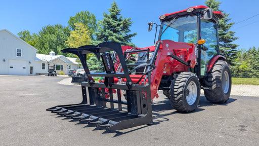 Storm root and brush grapple mounted on a red compact tractor front loader with the clamp open on a paved lot