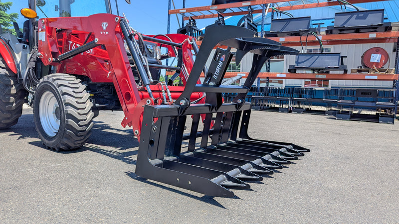 Storm root and brush grapple on a red tractor loader, tilted forward with the tines lowered toward the ground