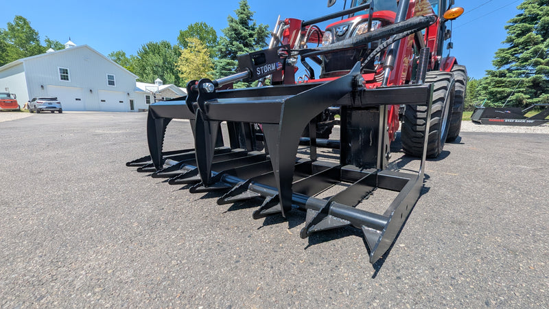 Storm root and brush grapple on a loader arm, side three-quarter view showing the spaced tines and top clamp