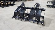 Storm two-cylinder root and brush grapple on a shop floor, clamp open, showing the two cylinders and the flat tine bank