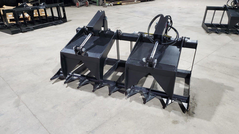 Storm two-cylinder root and brush grapple on a shop floor, clamp open, showing the two cylinders and the flat tine bank