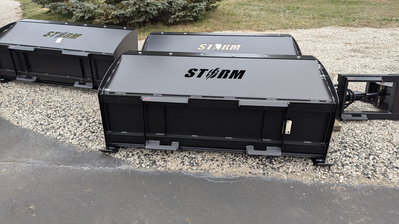 Storm snow pushers parked on gravel, three-quarter view of the boxed body and the top cap