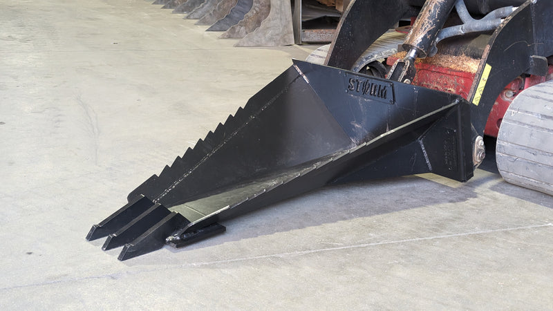 Storm stump bucket mounted on a skid steer, teeth forward on gravel