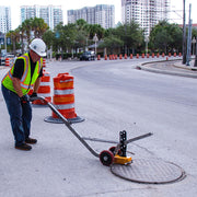 Operator rolling a manhole cover away on the aluminum dolly in a coned street