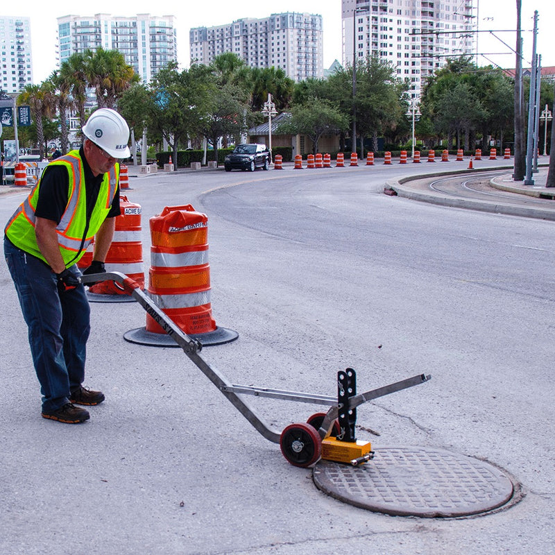 Operator rolling a manhole cover away on the aluminum dolly in a coned street