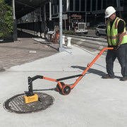Operator lifting a manhole cover with the curved steel dolly on a sidewalk