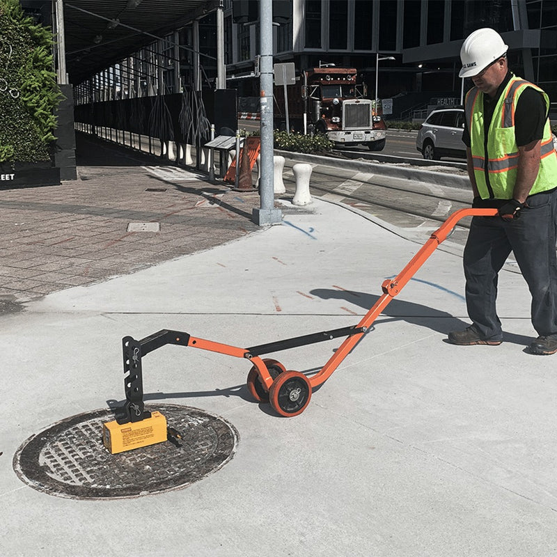 Operator lifting a manhole cover with the curved steel dolly on a sidewalk